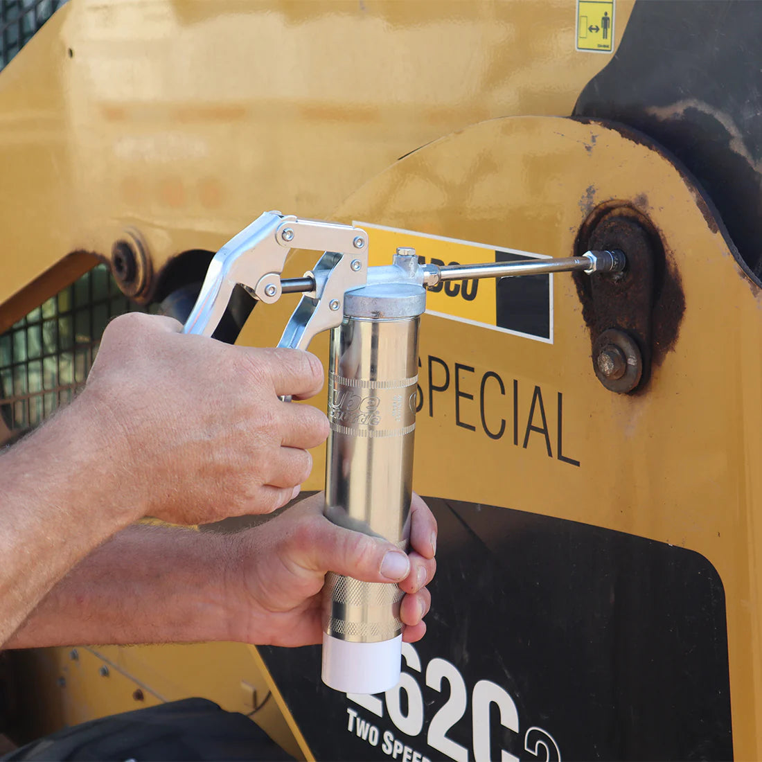 A person holding a grease gun, greasing a tractor.